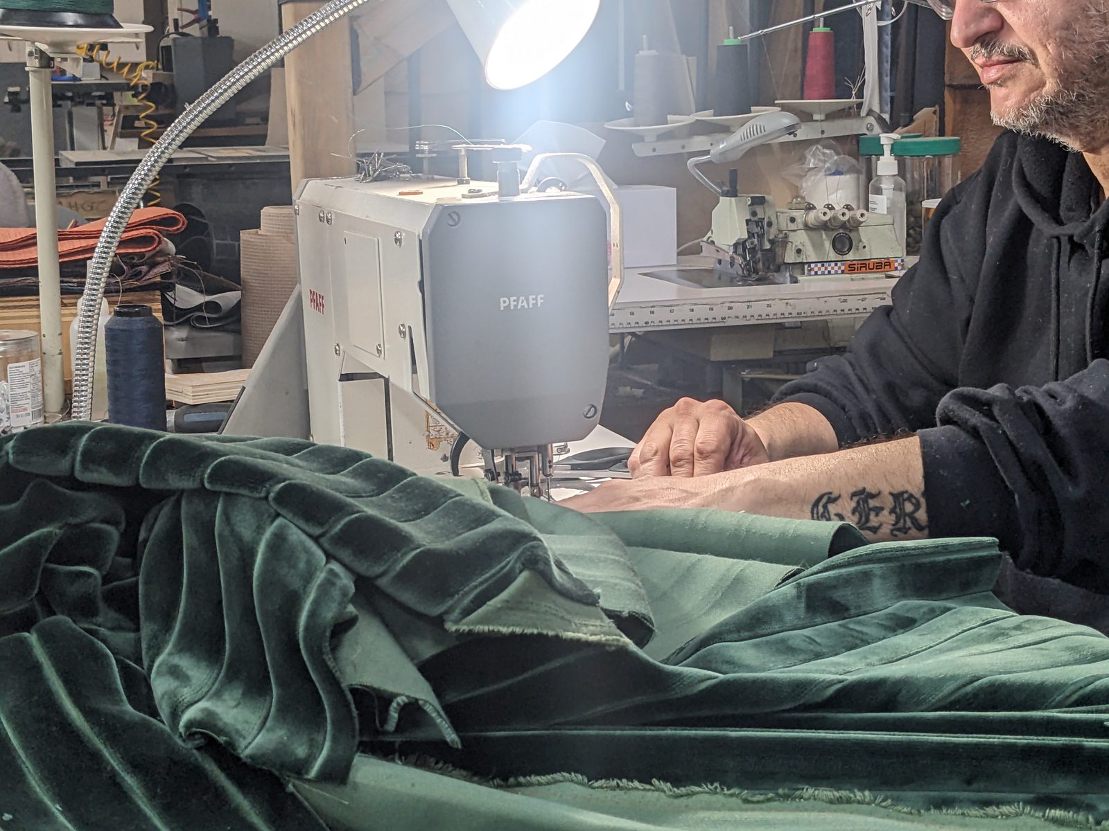 Upholsterer sewing green corduroy at a Pfaff machine under a work lamp
